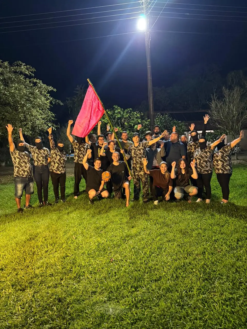 Turma do A Arte da Guerra Start reunida no campo à noite com a bandeira erguida
